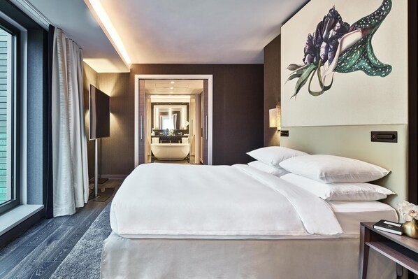 Habitación de hotel con una cama grande, un televisor de pantalla plana, un baño con bañera y un cuadro en la pared.