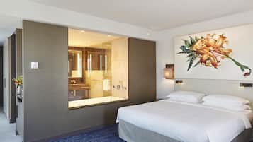 Una habitación de hotel con una cama grande, un baño con cabina de ducha de vidrio y un cuadro de una flor colgado en la pared.