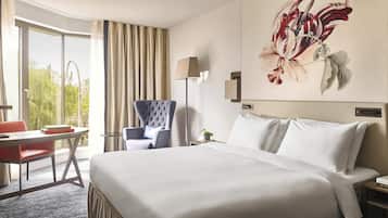 Habitación de hotel con una cama grande, un escritorio con silla, una lámpara y un cuadro en la pared.