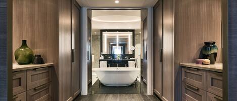 A modern bathroom with a freestanding bathtub, wooden cabinetry, and a marble floor.