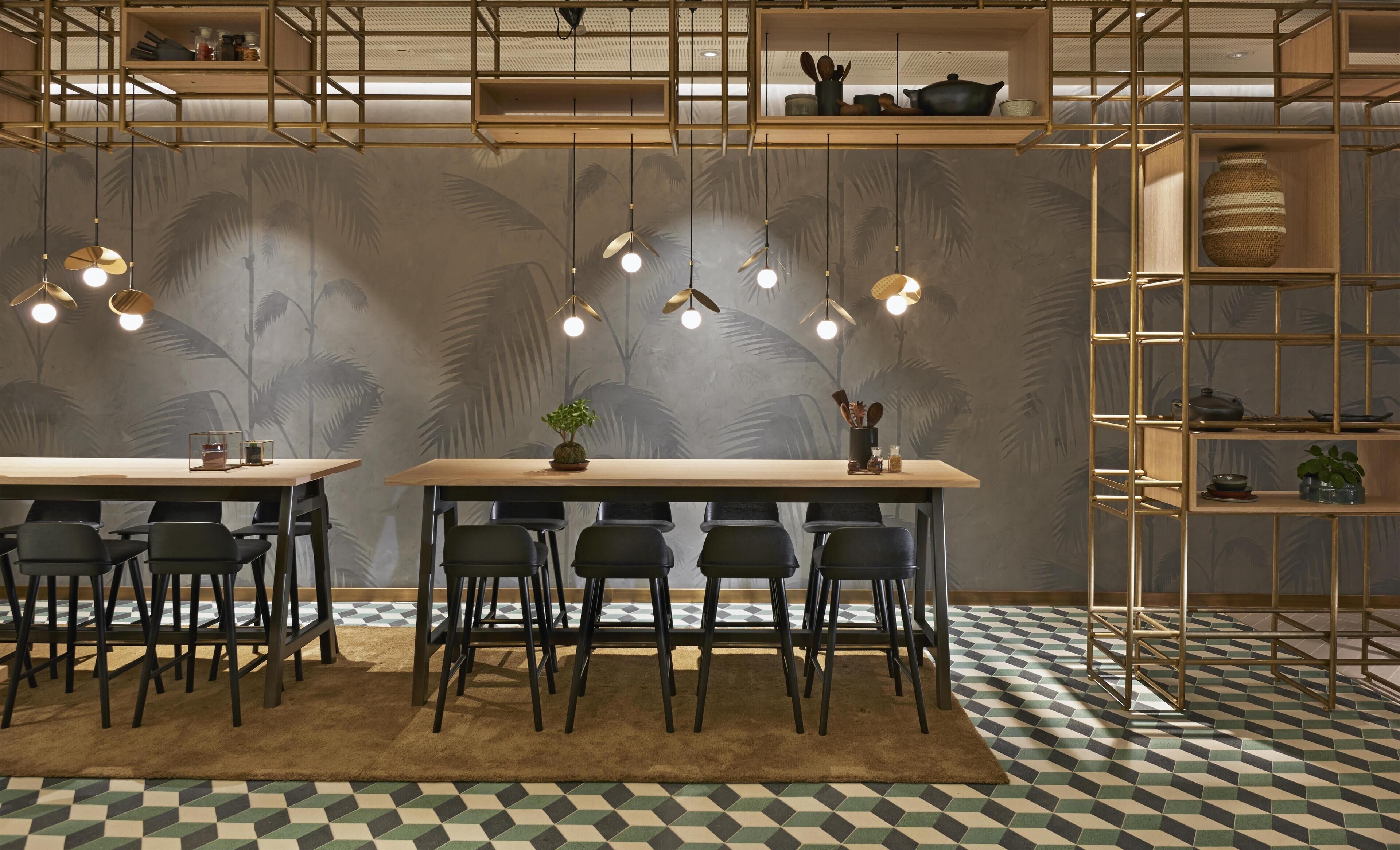 Un espace repas comprenant deux tables, des chaises, des luminaires suspendus et un sol à motifs.
