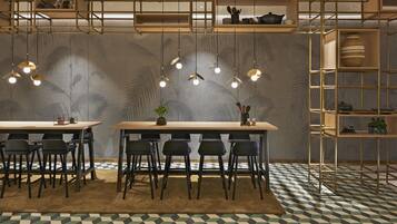 Un espace repas comprenant deux tables, des chaises, des luminaires suspendus et un sol à motifs.