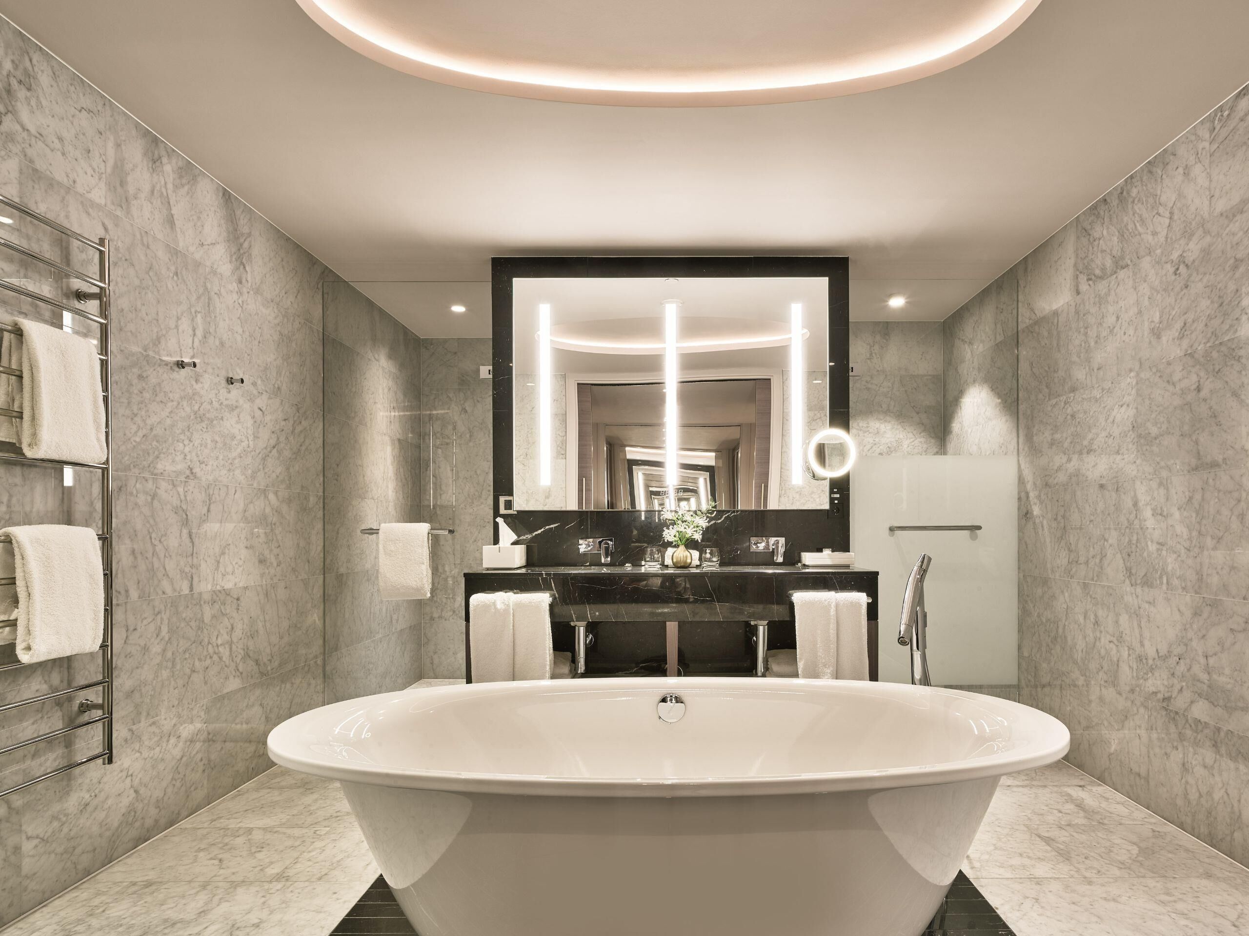 Een moderne badkamer met een vrijstaand bad, een grote spiegel en een handdoekrek.