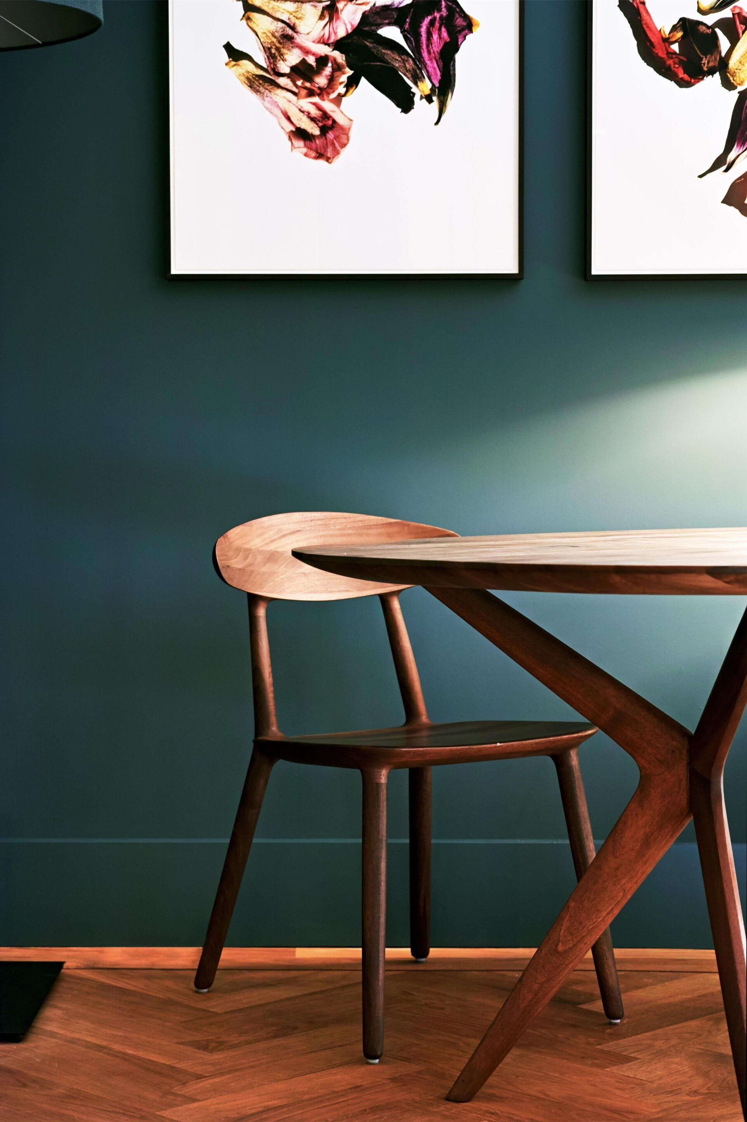 A dining area with a wooden table and chairs, framed artwork on the wall, and a dark teal wall.