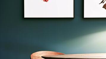 A dining area with a wooden table and chairs, framed artwork on the wall, and a dark teal wall.