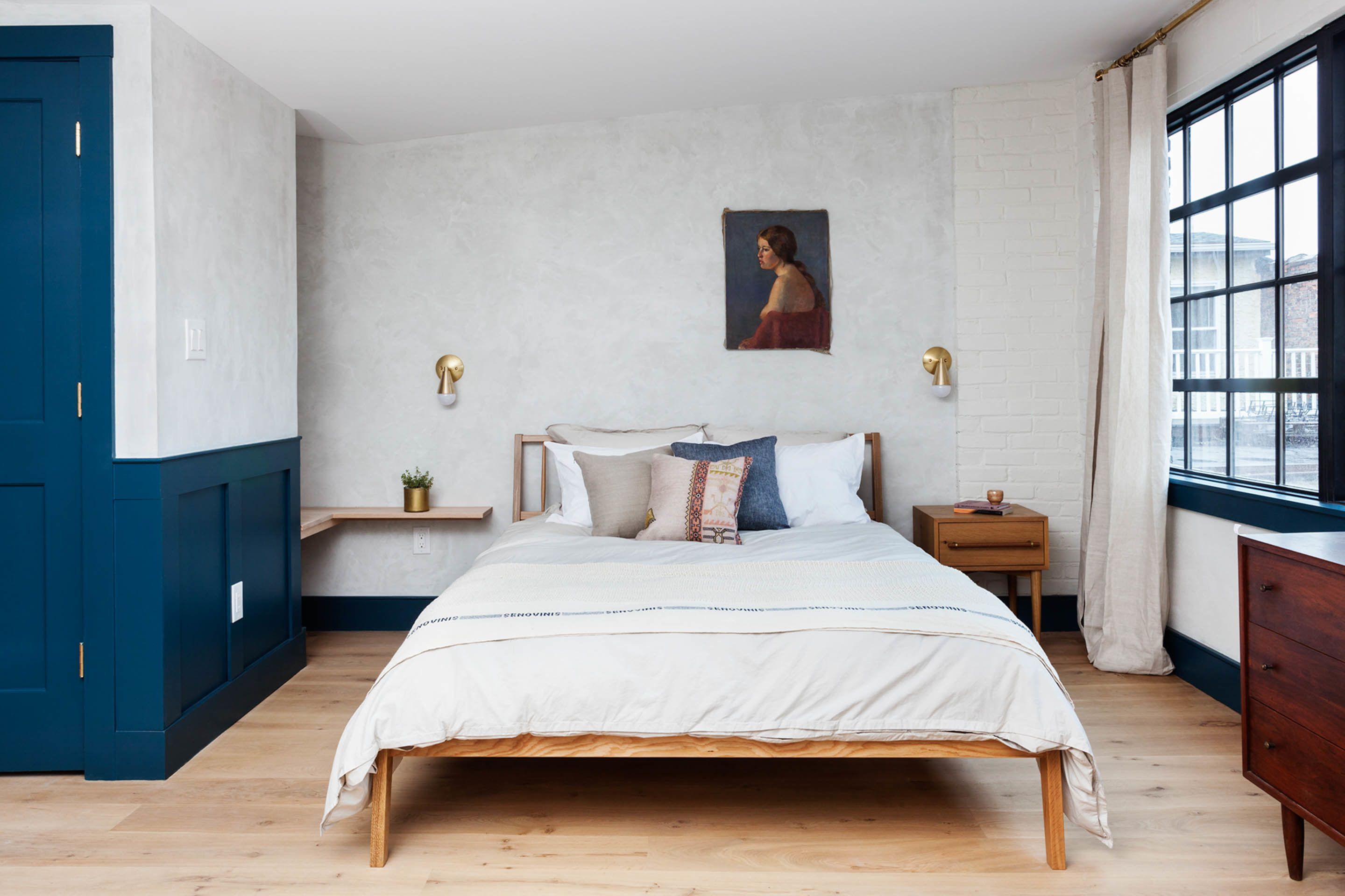 A bedroom with a wooden bed, a nightstand, a dresser, a window with curtains, and a painting on the wall.