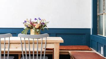 A dining area with a wooden table, two grey chairs, a bench, and a vase of flowers on the wall.