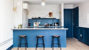 A modern kitchen with a blue accent wall, a white countertop, and three black bar stools. - Lokal Hotel - Old City (Philadelphia)
