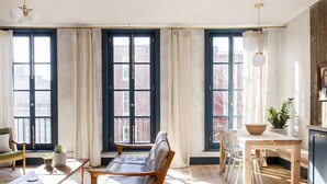 Un salón amplio con ventanas grandes, un sofá, una mesa de comedor y un televisor.