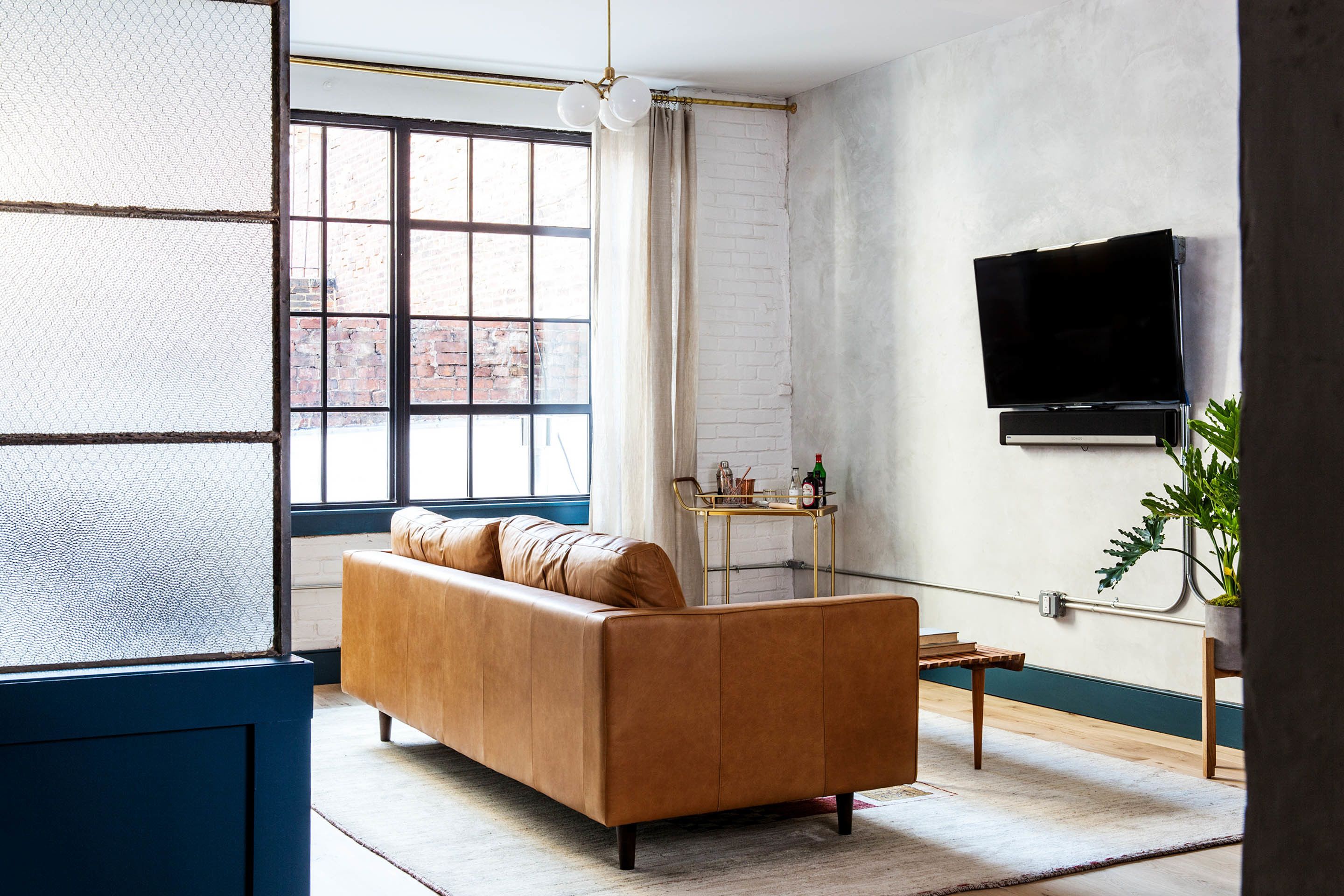 Una sala de estar con un sofá de cuero, un televisor montado en la pared y una ventana con vistas al exterior.