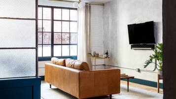 Una sala de estar con un sofá de cuero, un televisor montado en la pared y una ventana con vistas al exterior.