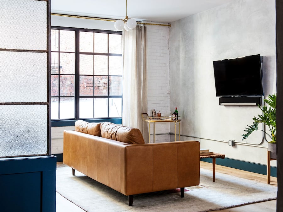 Una sala de estar con un sofá de cuero, un televisor montado en la pared y una ventana con vistas al exterior.