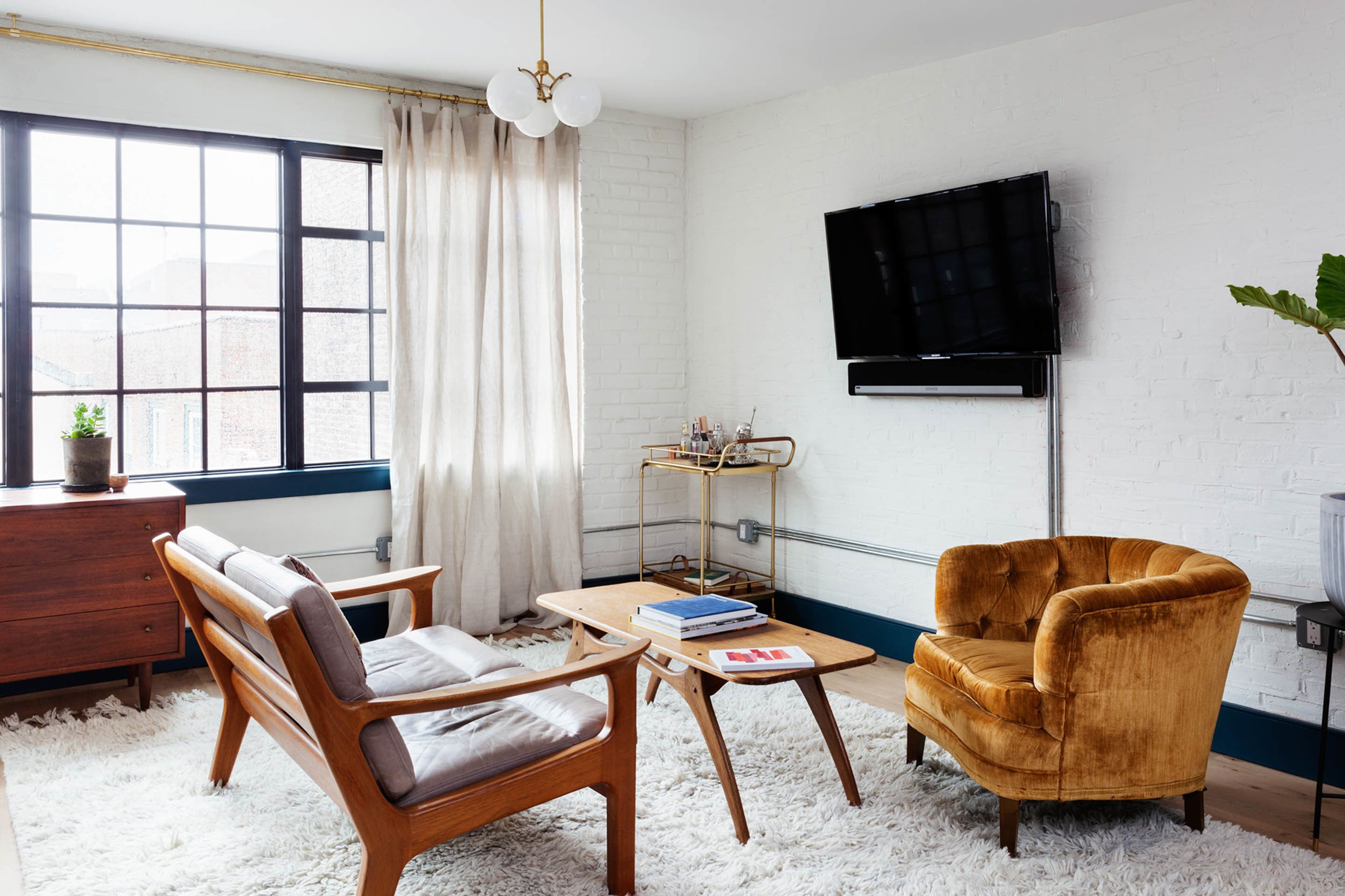 A living room with a sofa, armchair, coffee table, and a TV mounted on the wall.