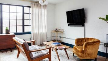 A living room with a sofa, armchair, coffee table, and a TV mounted on the wall.