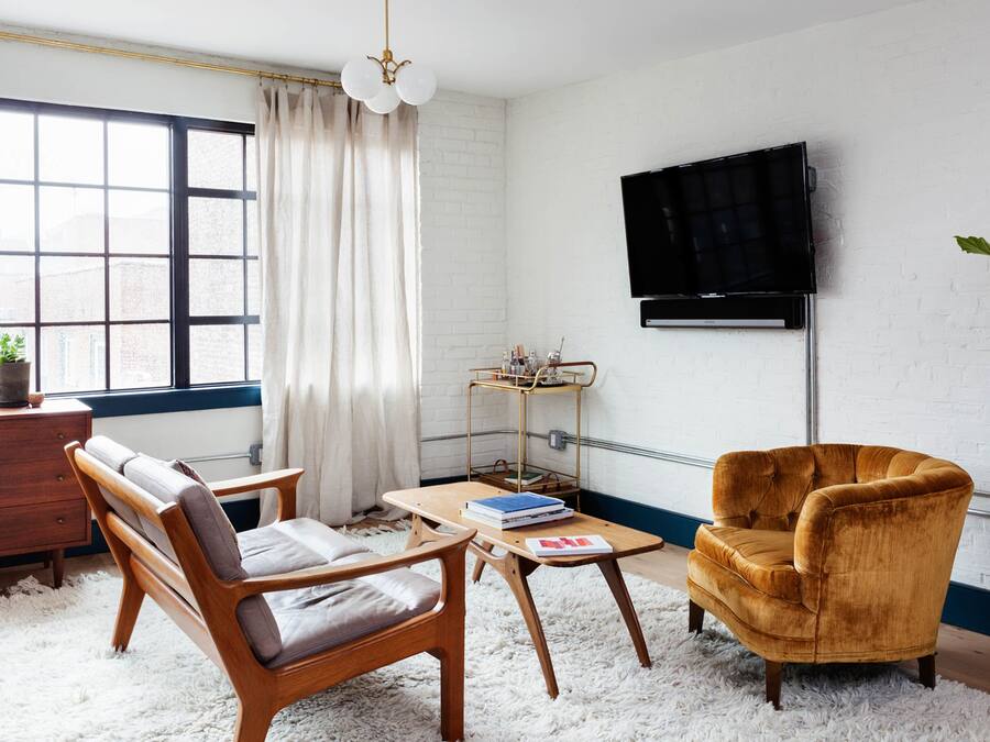 A living room with a sofa, armchair, coffee table, and a TV mounted on the wall.