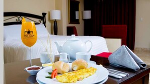 A hotel room with a neatly made bed, a dining table with breakfast items including eggs, bread, and a glass of orange juice. - HACIENDA SAN JUAN RESORT   (San Juan Bautista)