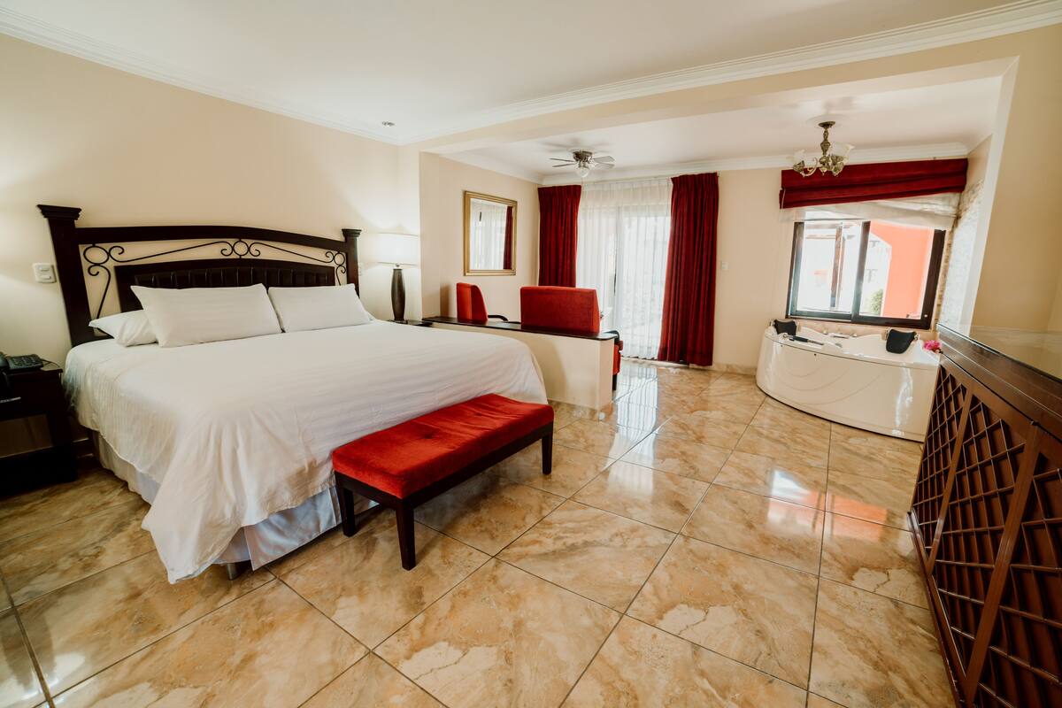Habitación de hotel con una cama grande, un banco, un escritorio y una ventana con cortinas.