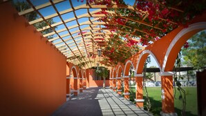 A covered walkway with arches and a pergola overhead, surrounded by orange walls and greenery. - HACIENDA SAN JUAN RESORT   (San Juan Bautista)