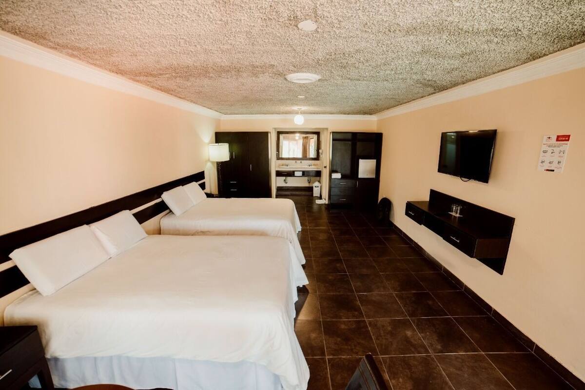 Habitación de hotel con dos camas, televisión, escritorio y baño a la vista.