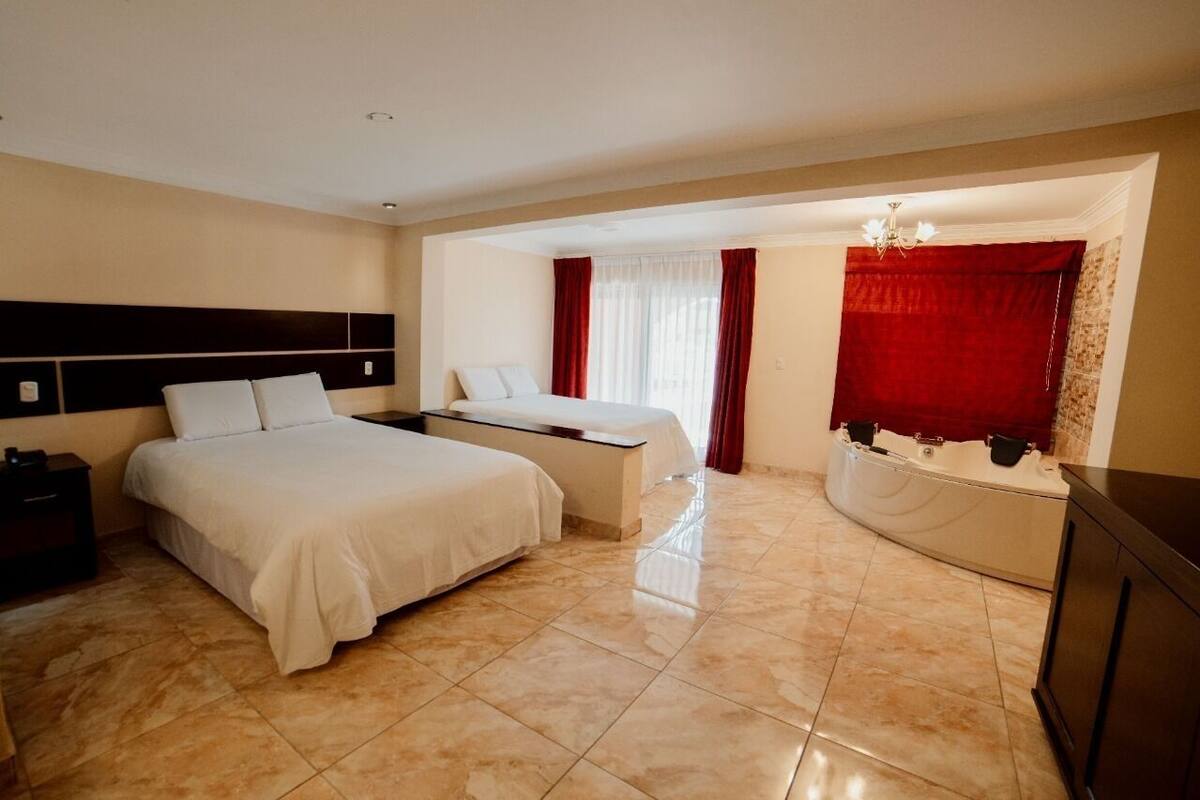Una habitación de hotel con una cama grande, una cama más pequeña, un tocador con espejo y una bañera.