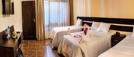 A hotel room with two beds, a desk with a fan, a mirror, and a door.