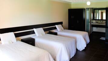 Habitación de hotel con dos camas individuales, un armario de madera oscura, un baño con espejo y lavamanos, y una lámpara en el techo.