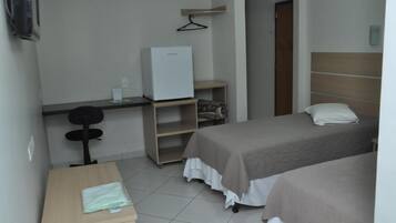 Een hotelkamer met twee bedden, een bureau met stoel, een koelkast en een kledingkast.