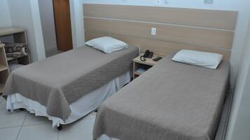 A hotel room with two single beds, a bedside table with a phone, and a small shelf with a blanket.