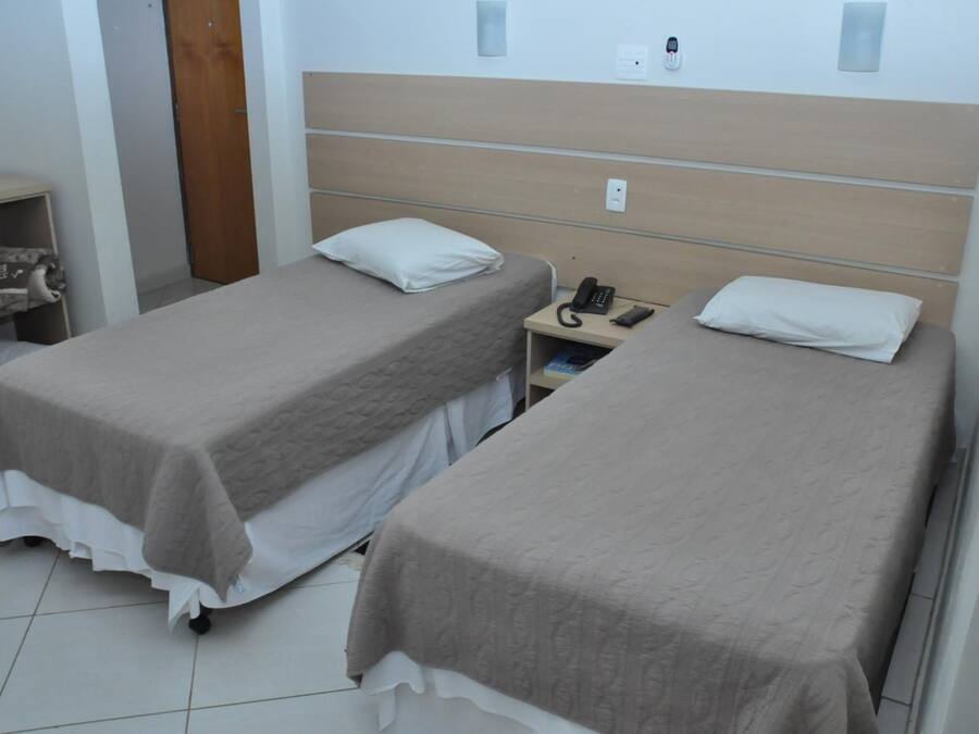 A hotel room with two single beds, a bedside table with a phone, and a small shelf with a blanket.