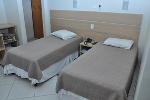 Habitación de hotel con dos camas individuales, una mesita de noche con teléfono y un estante pequeño con una manta.