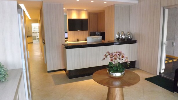 Un moderno vestíbulo de hotel con un mostrador de recepción, un televisor de pantalla plana y una orquídea decorativa sobre una mesa redonda.