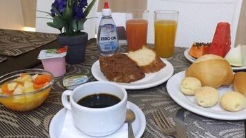 En frukostuppdukning med en kopp kaffe, juice, en tallrik mat och en blomvas.