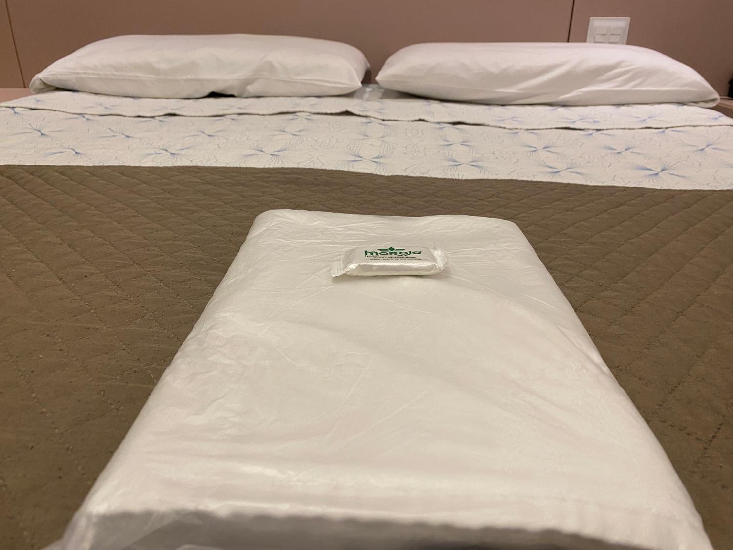 A bed with a white mattress and a pillow, a brown quilted blanket, and a small white object on the bed.