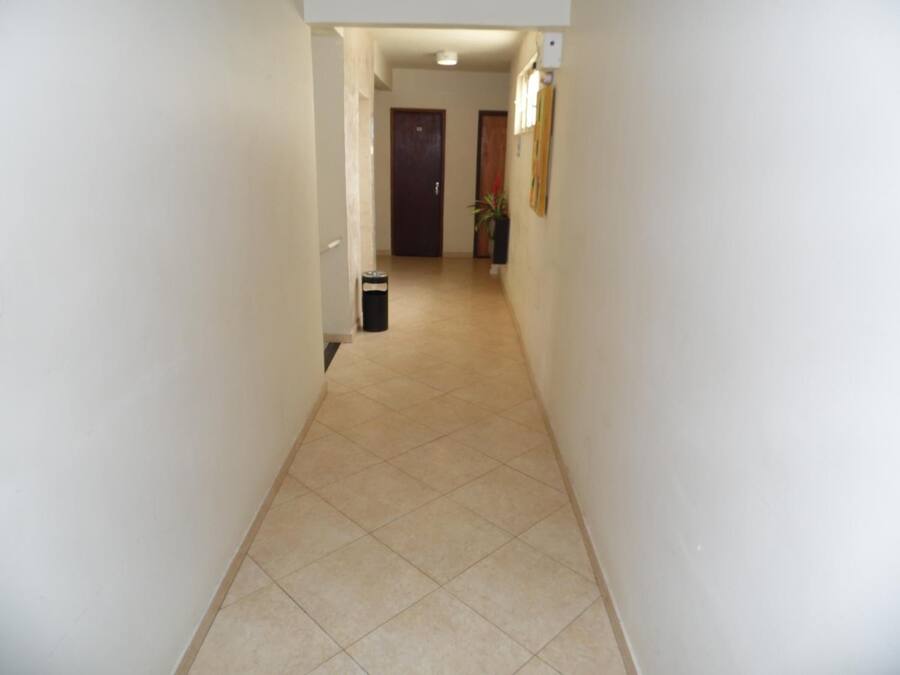 A narrow hallway with tiled flooring, a trash bin, and a door at the end.