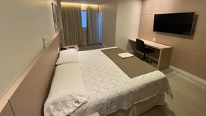 Una habitación de hotel con cama, escritorio, silla, televisor y cortinas.