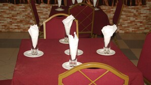 Una mesa de comedor dispuesta con servilletas blancas y cristalería transparente, rodeada de sillas tapizadas en rojo.