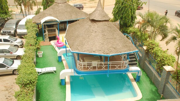 Una piscina con una estructura de techo de paja, un área de juegos pequeña y una zona de estar cubierta.