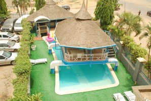 A swimming pool with a thatched roof structure, a small play area, and a covered seating area. - Peace Haven Hotel (Abuja)
