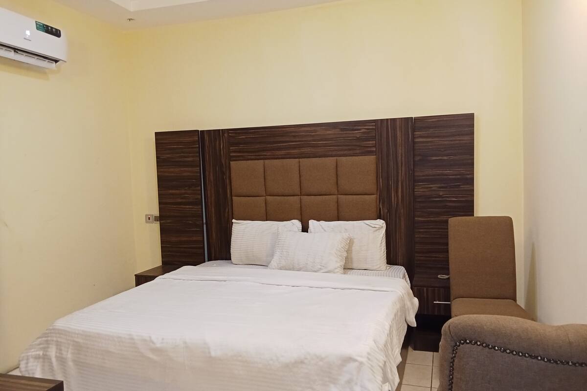 A hotel room with a large bed, a wooden headboard, a bedside table, and a chair.