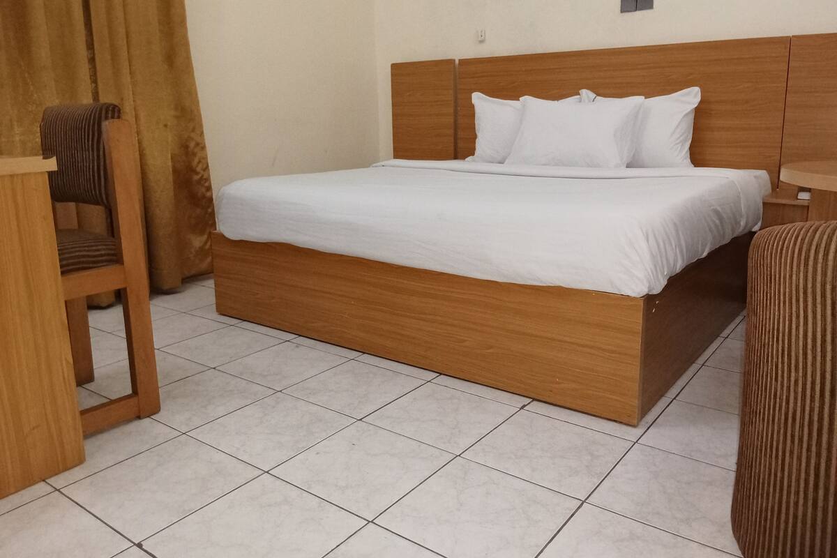 A single bed with a wooden headboard and white bedding in a room with tiled flooring.
