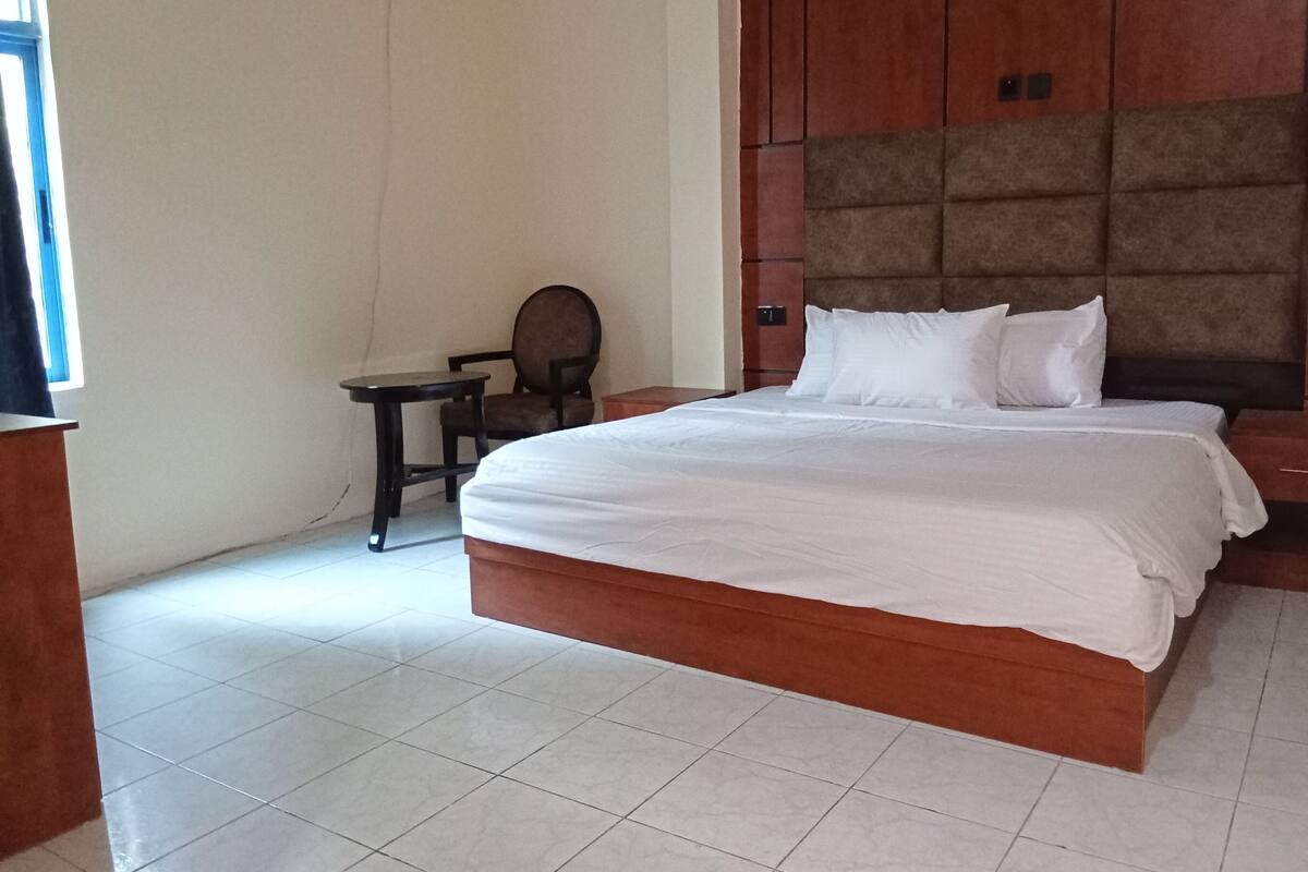 A hotel room with a large bed, a small table, a chair, and a nightstand.