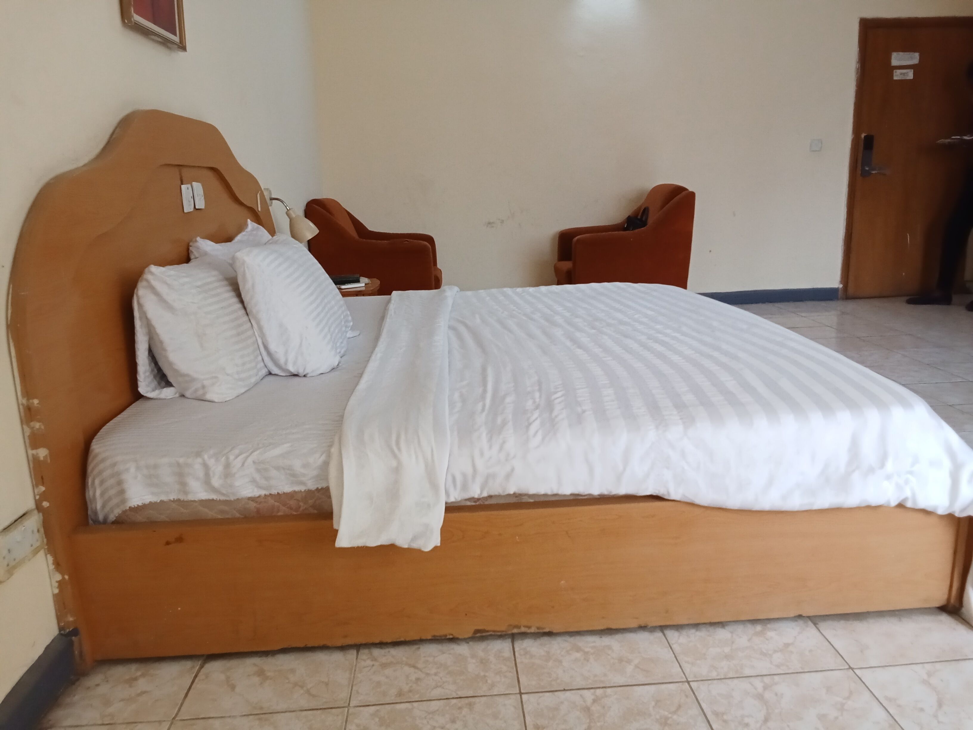A bed with a wooden headboard, two pillows, and a white blanket. There are two chairs against the wall.
