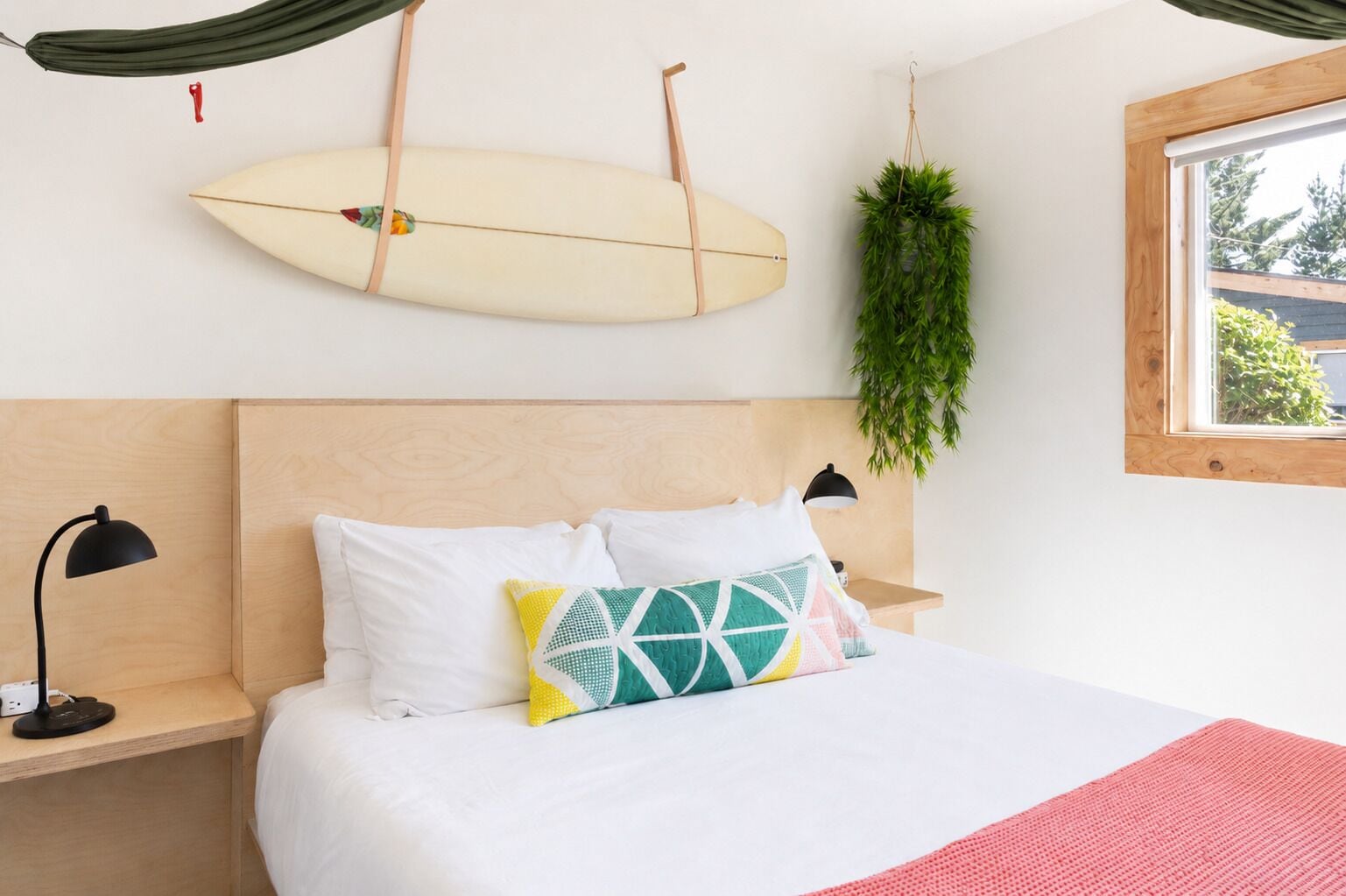 Une chambre avec un lit, des lampes de chevet, une planche de surf accrochée au mur et une fenêtre donnant sur un beau paysage.