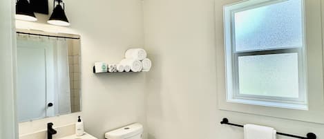 A small, clean bathroom with a white sink, toilet, and mirror. There is a window with frosted glass and a towel rack with a white towel.