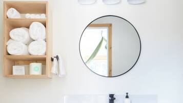 Une salle de bain avec un meuble-lavabo en bois, un miroir rond et trois appliques murales.