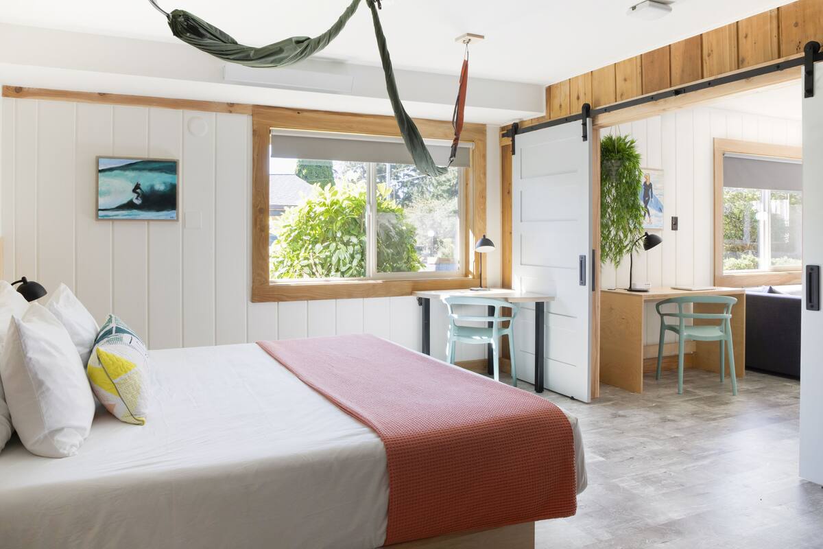 A bedroom with a bed, a desk, and a chair. There is a window with a view of greenery outside.