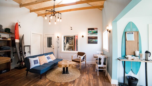 A cozy living room with a blue sofa, wooden coffee table, and a surfboard on the wall. - Gravity Haus Westport (Westport)
