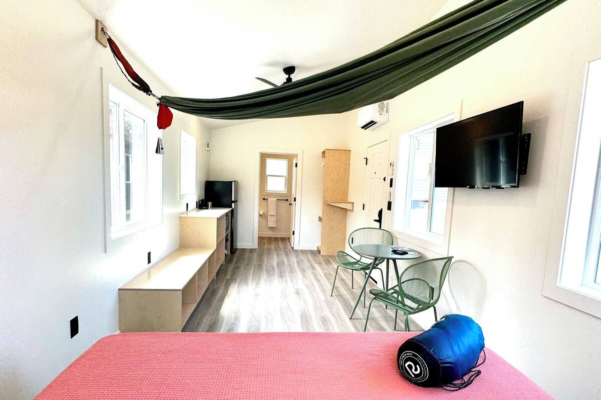 A compact hotel room with a bed, a TV, a kitchenette, and a dining area with chairs.