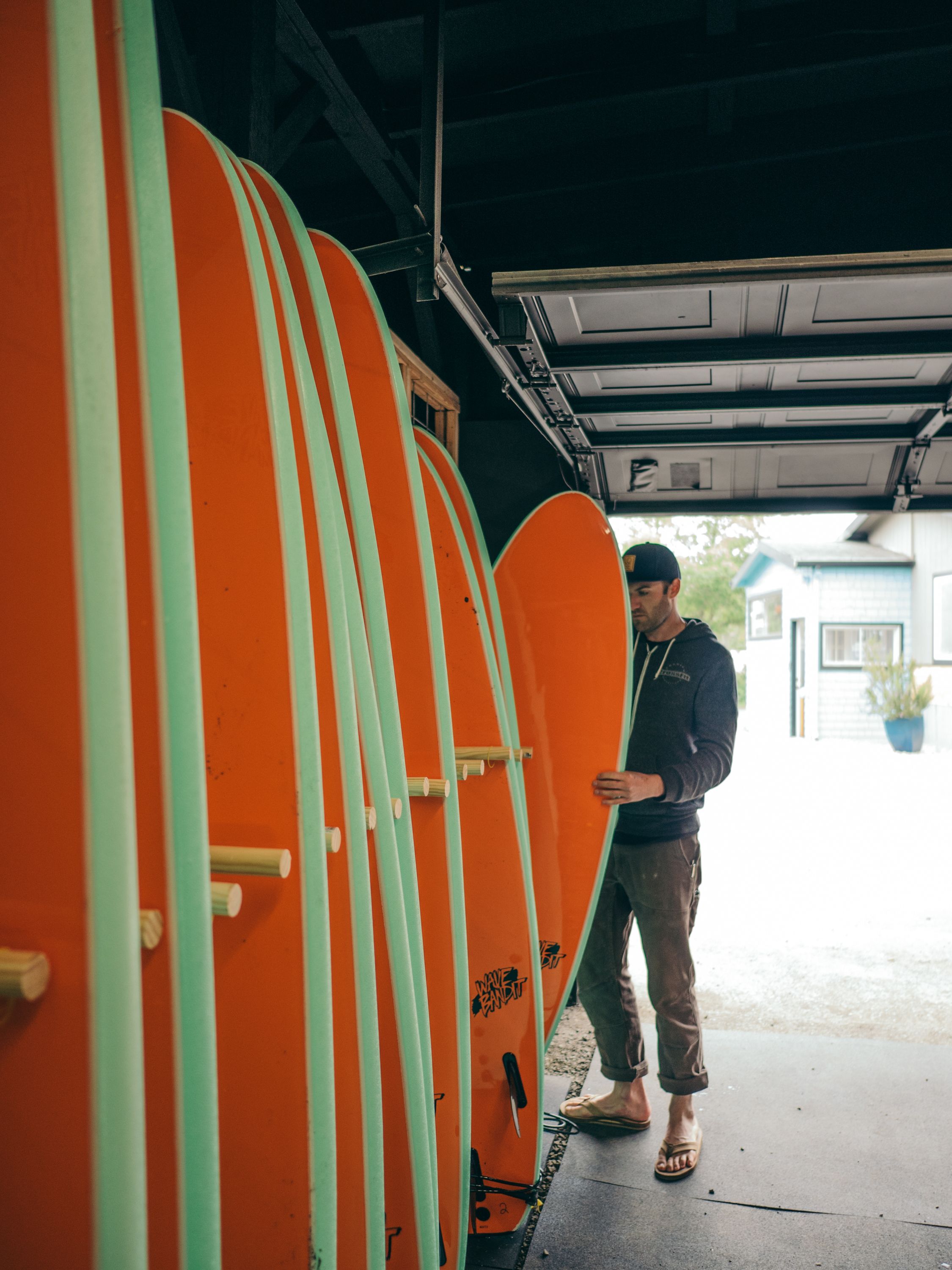 Una persona de pie al lado de varios botes de surf en un espacio que se asemeja a un garaje.