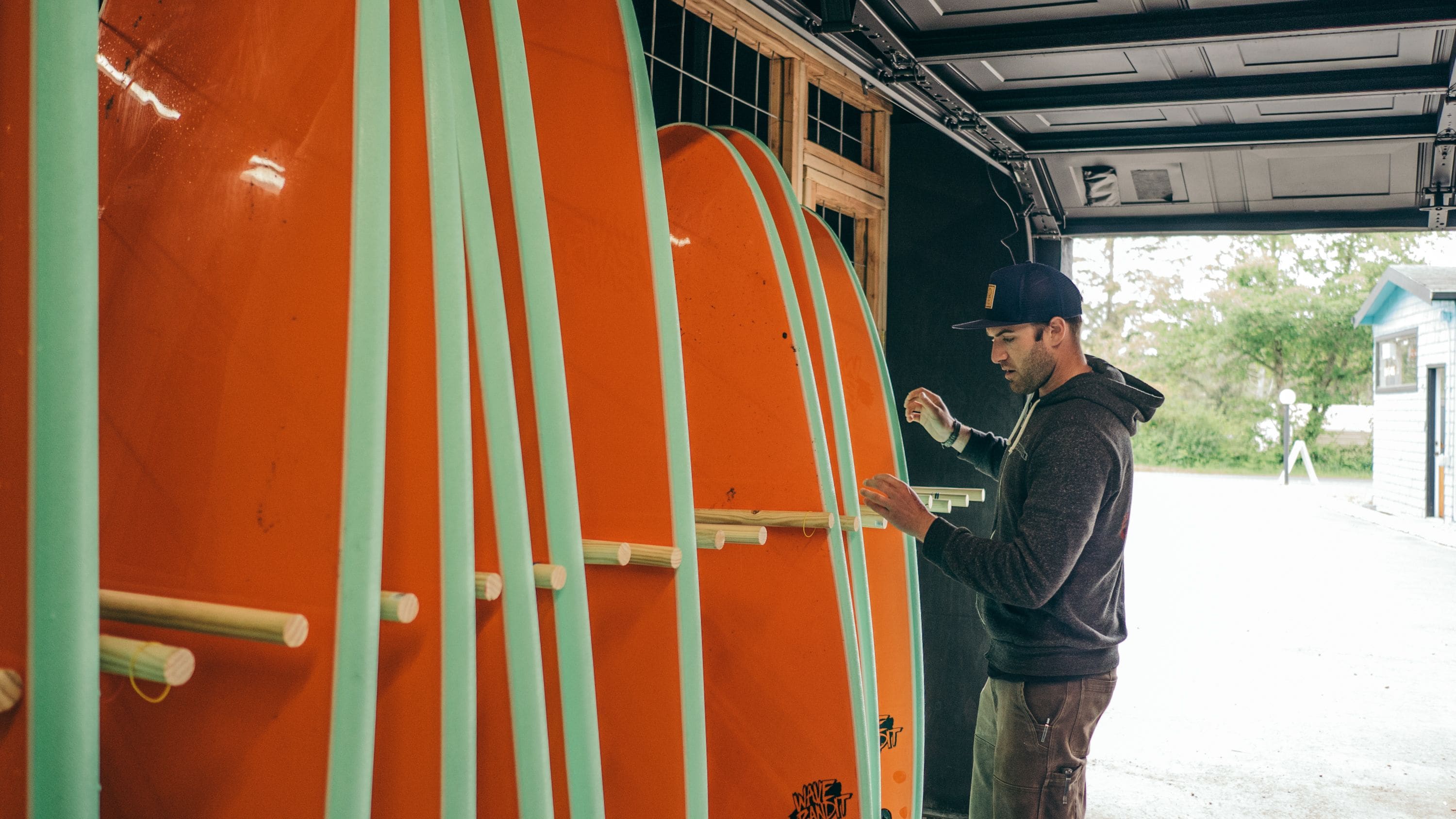 A person standing next to a large orange and green structure, possibly a vehicle or equipment, with a window and a door.